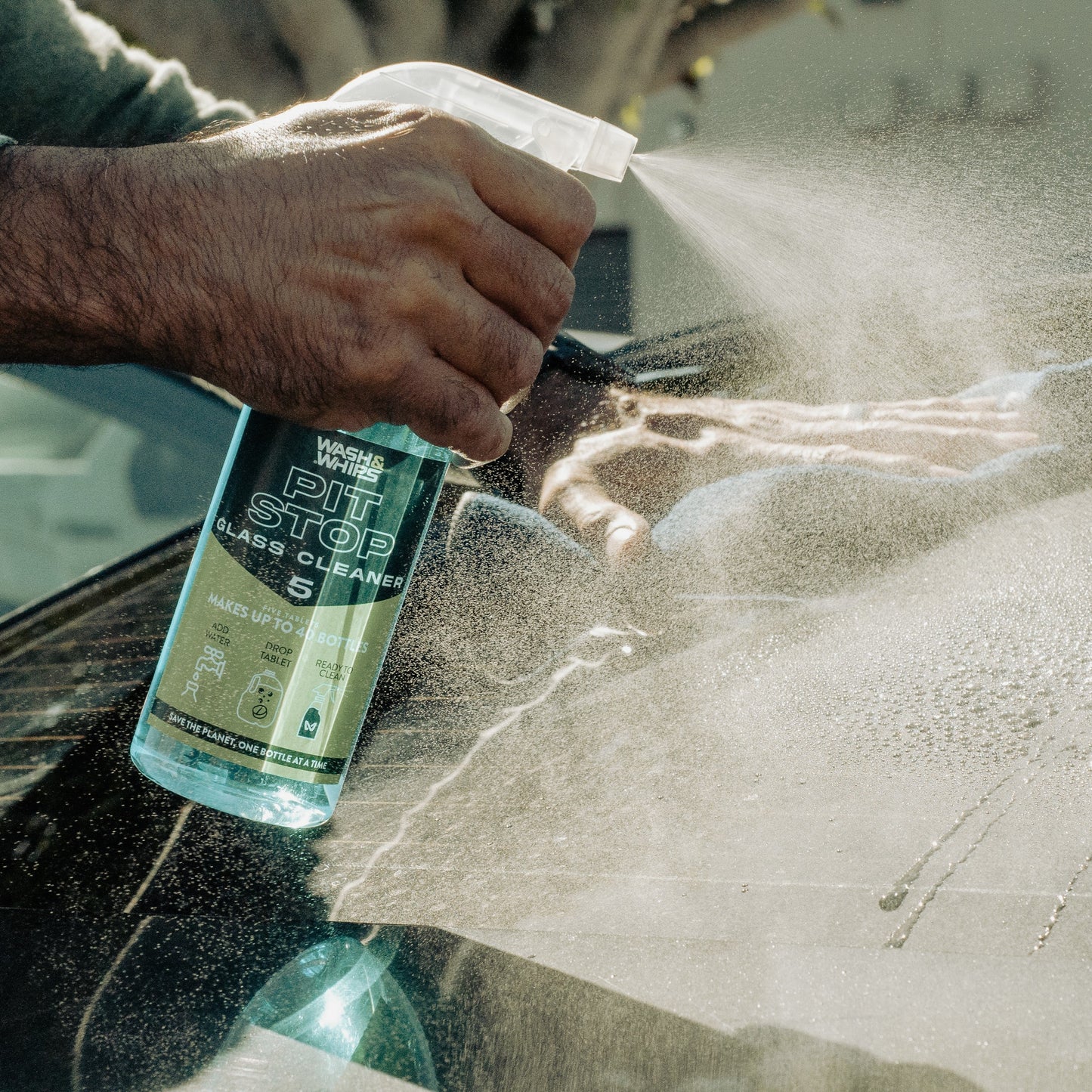 Person cleaning a car window with a spray bottle labeled 'Pit Stop Glass Cleaner'.