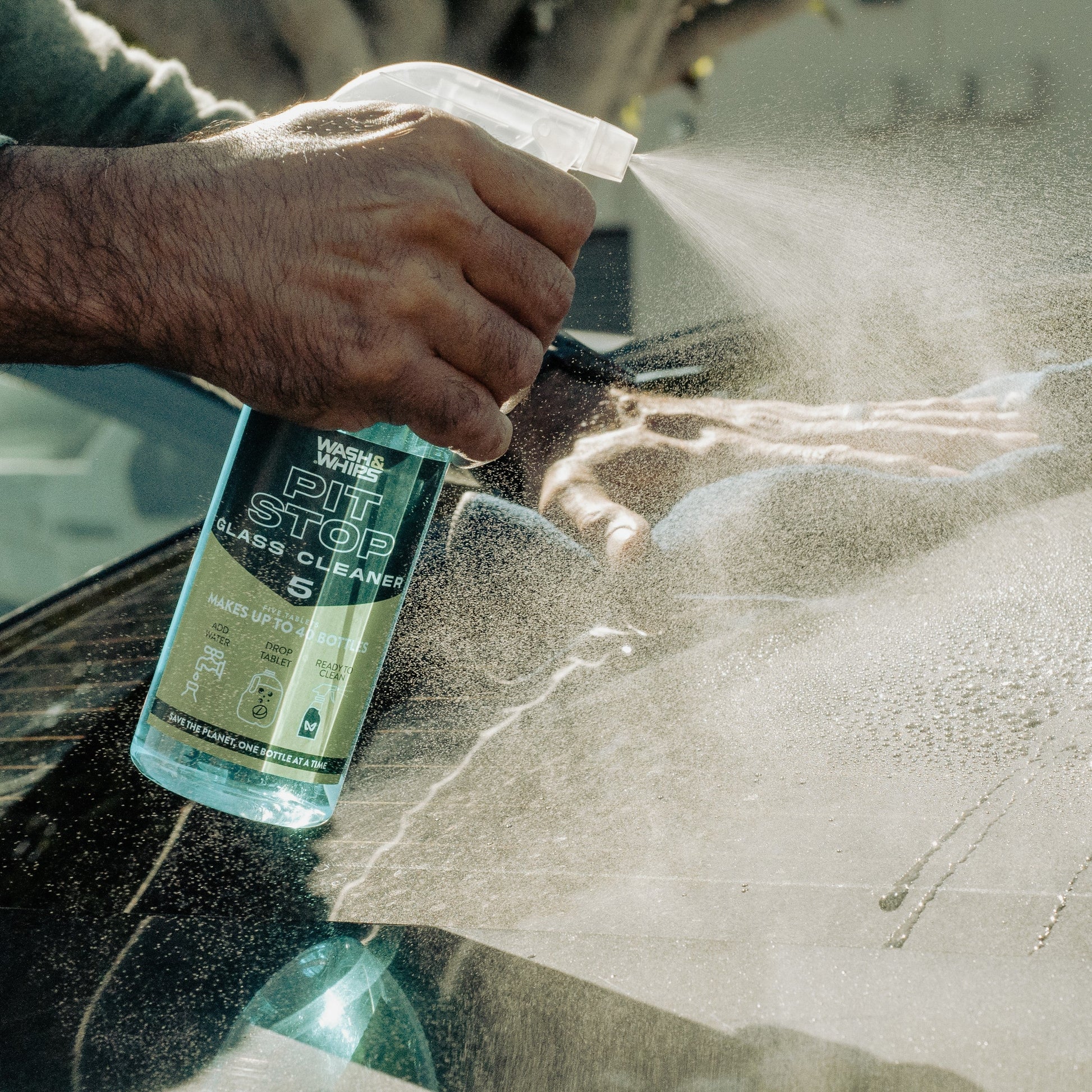 Person cleaning a car window with a spray bottle labeled 'Pit Stop Glass Cleaner'.