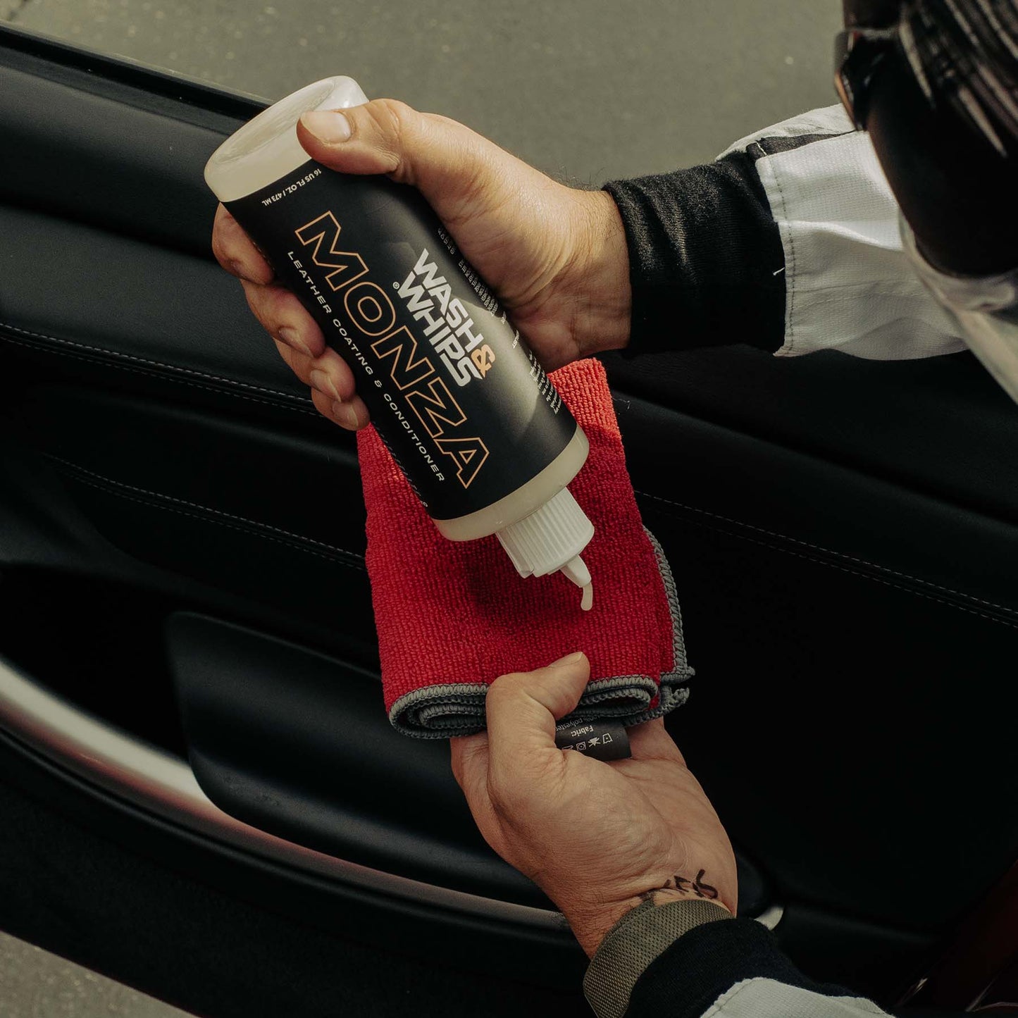 Person holding a can of 'Wash Monza' with a red towel, cleaning a car.