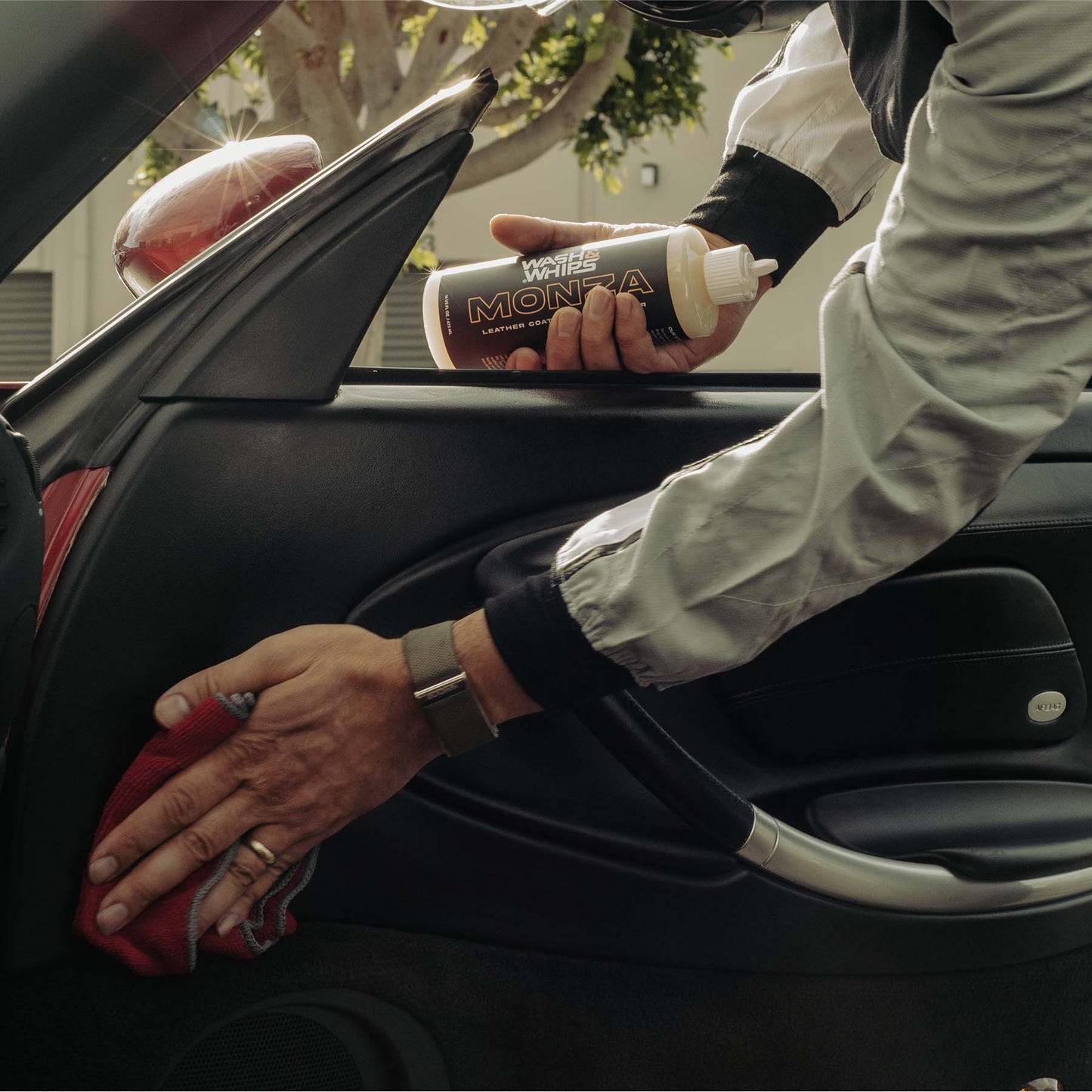 Person cleaning a car interior with a red cloth and a bottle of detailing product.
