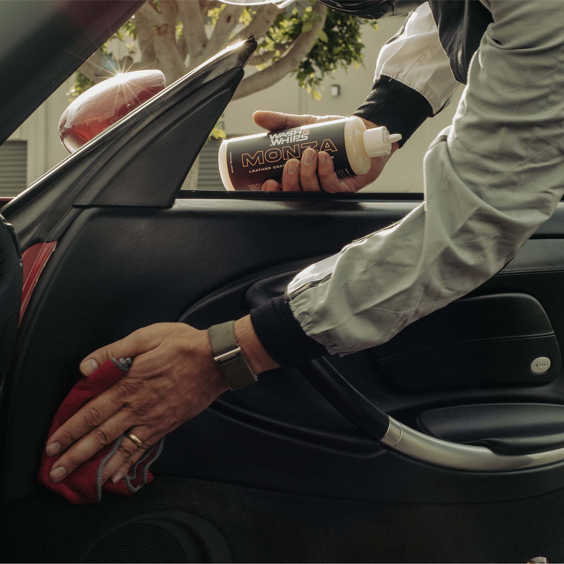 Person cleaning a car interior with a red cloth and a bottle of detailing product.