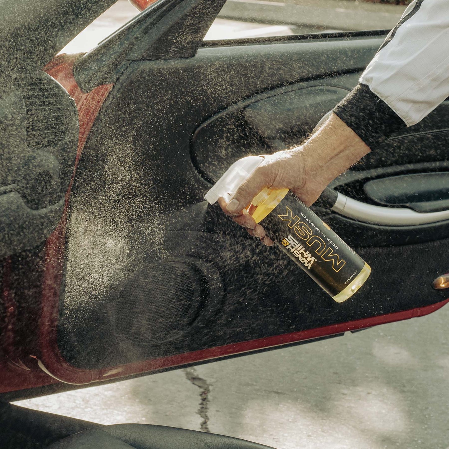 Person cleaning a car window with a spray bottle labeled 'Muc-Off'.