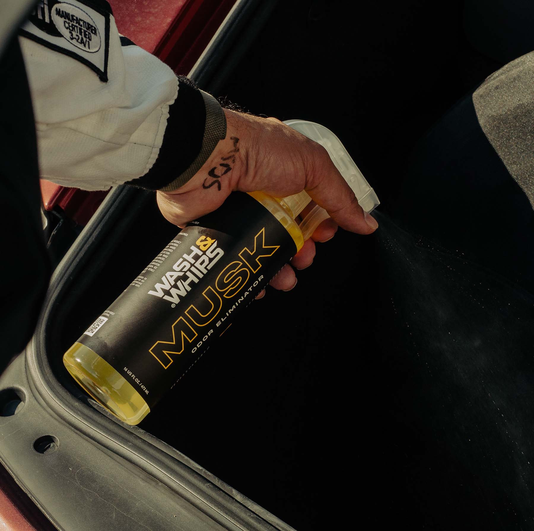 Person holding a can of Wash and Whips Musk spray near a car door.