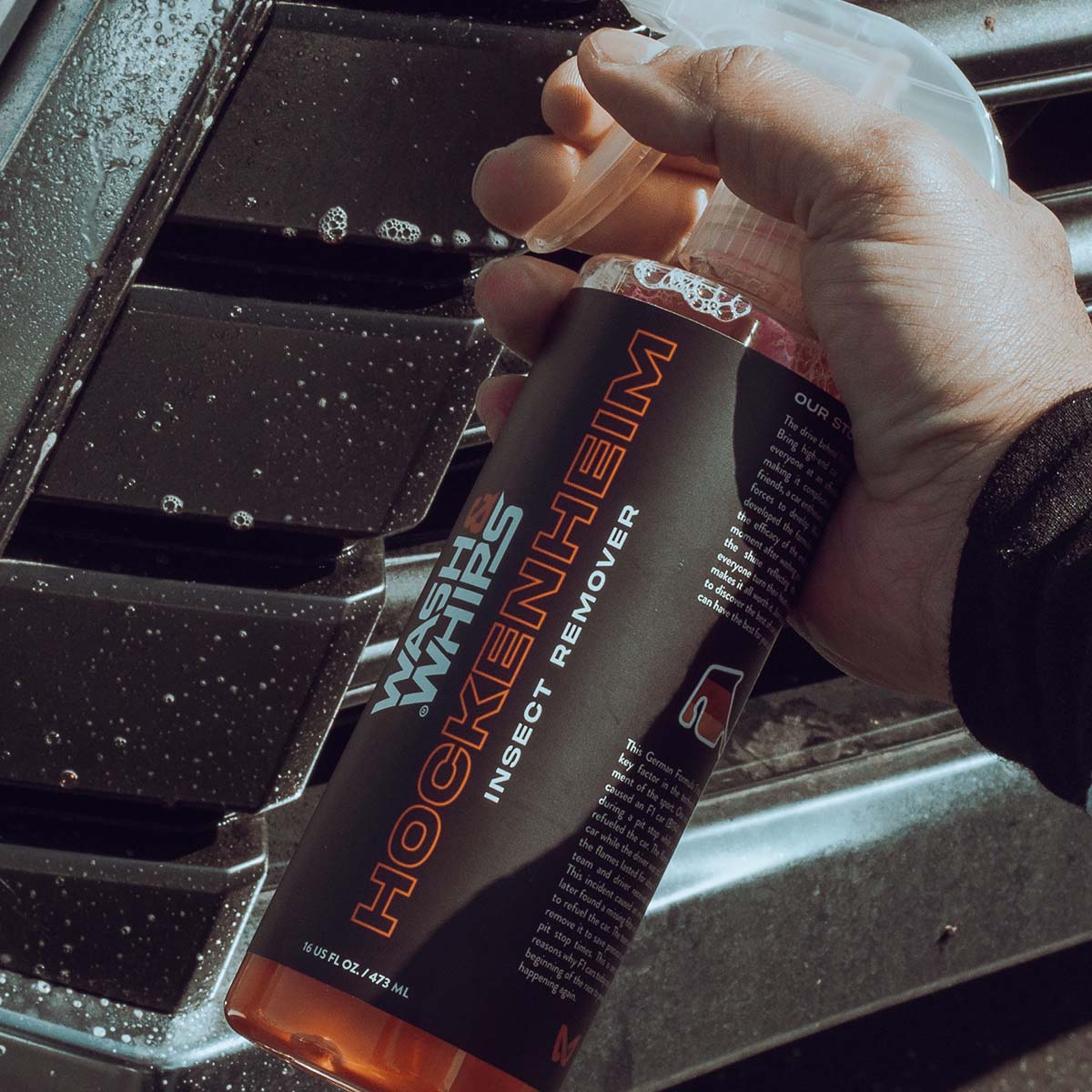Hand holding a bottle of Hockenheim insect remover over a car's air vent.