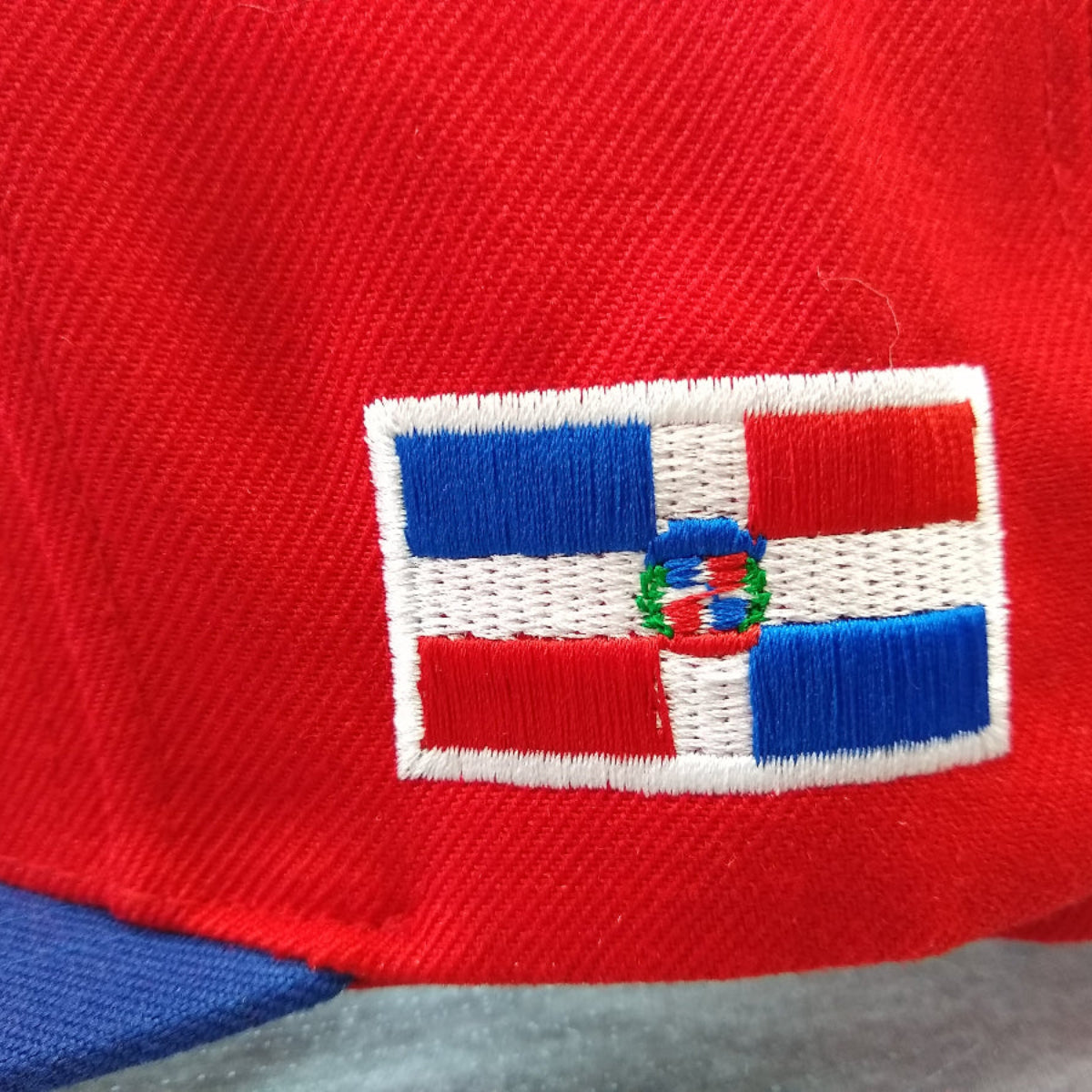 Close-up of a red cap with a Dominican Republic flag emblem featuring blue, white, and red colors.
