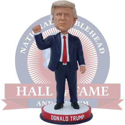 Bobblehead figure of Donald Trump in a suit with a red tie, standing in front of a 'National Bobblehead Hall of Fame and Museum' logo.