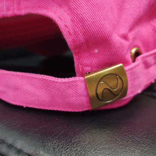 Close-up of a pink cap with a gold buckle on a dark surface