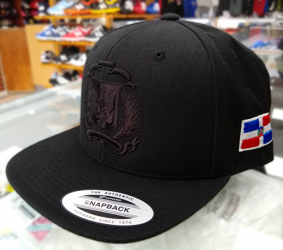 Black snapback cap with a logo and flag patch on a reflective surface.