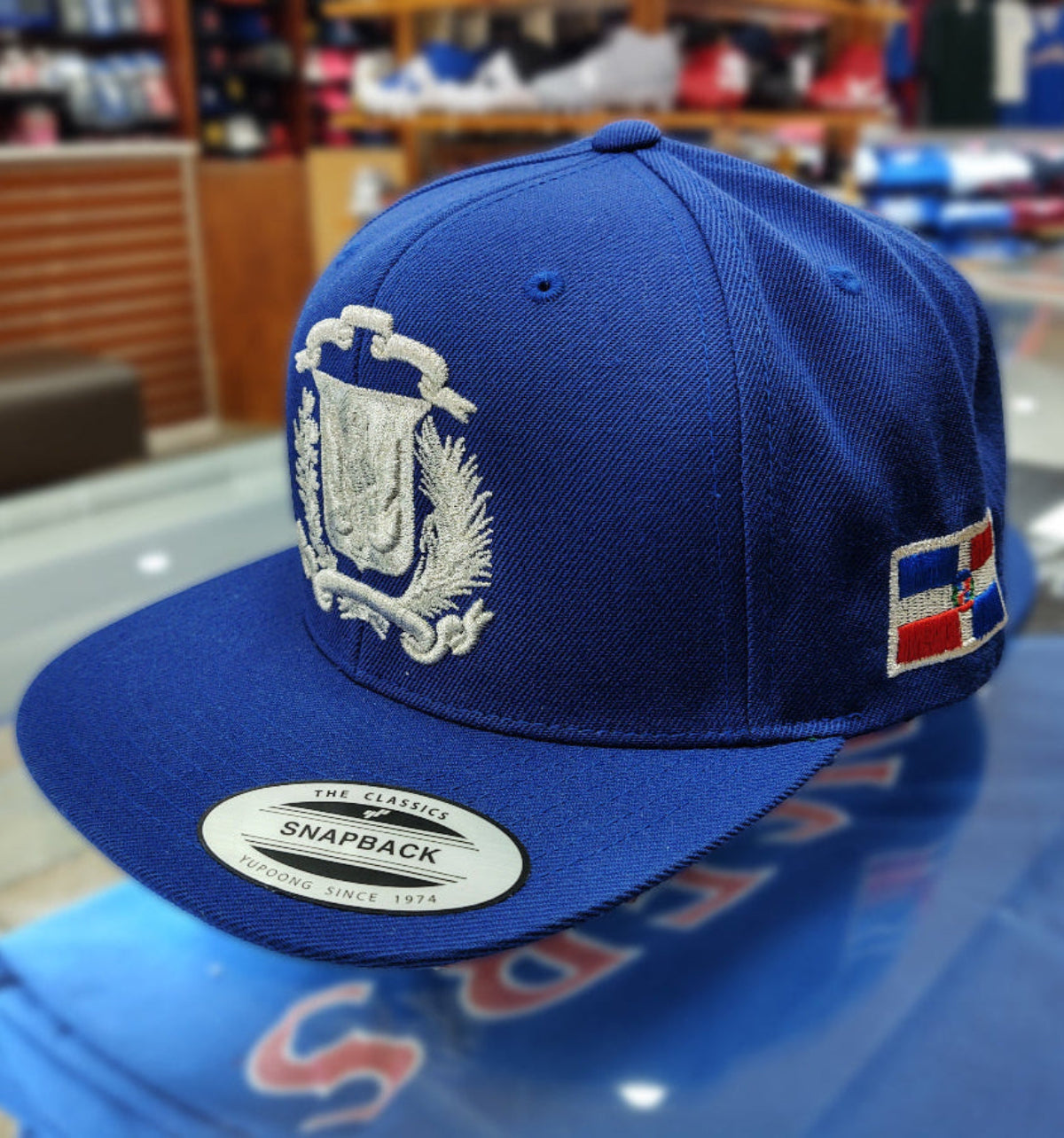 Blue snapback cap with a logo and text on a reflective surface