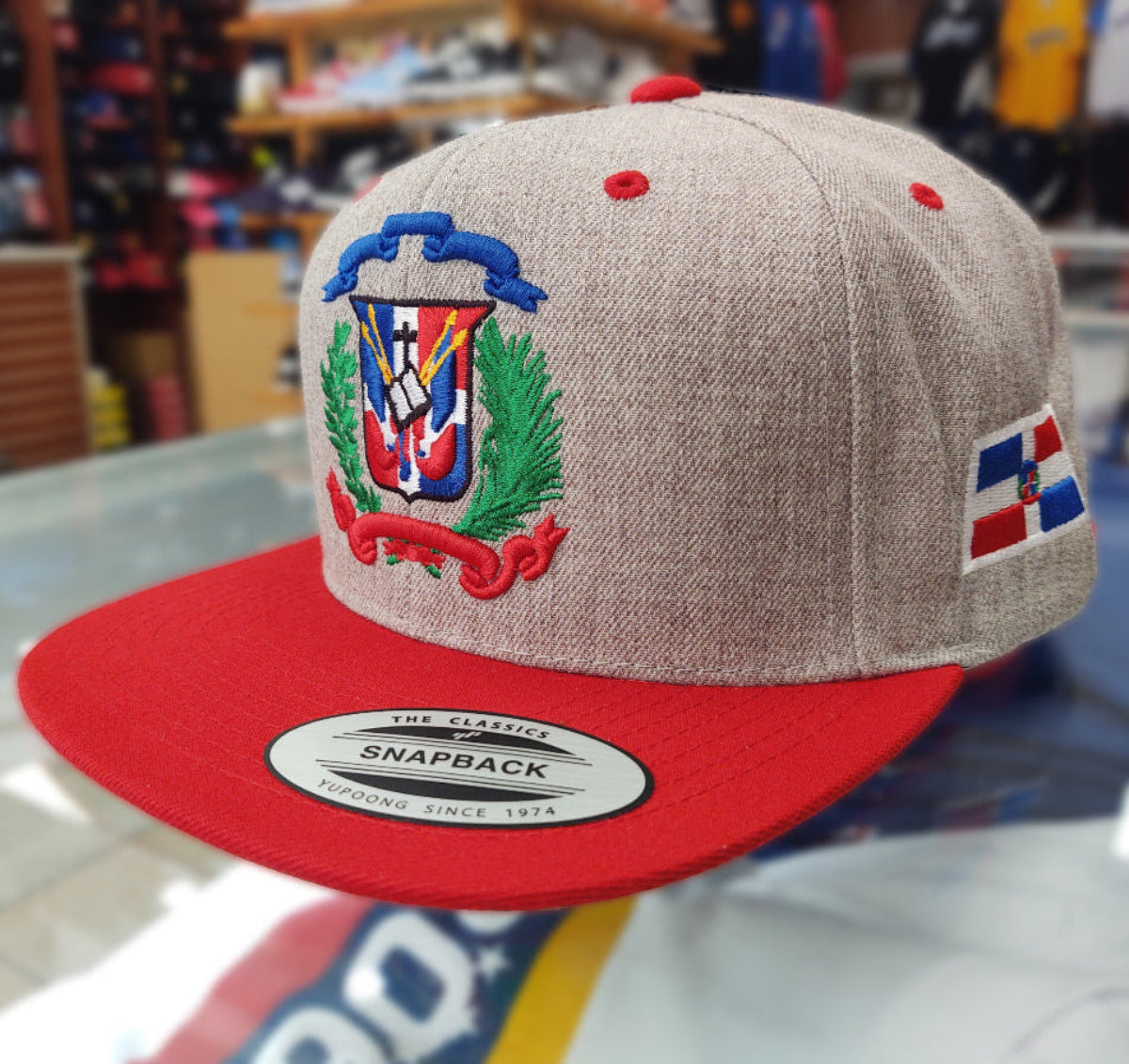 Beige and red snapback cap with a Dominican logo on a blurred background
