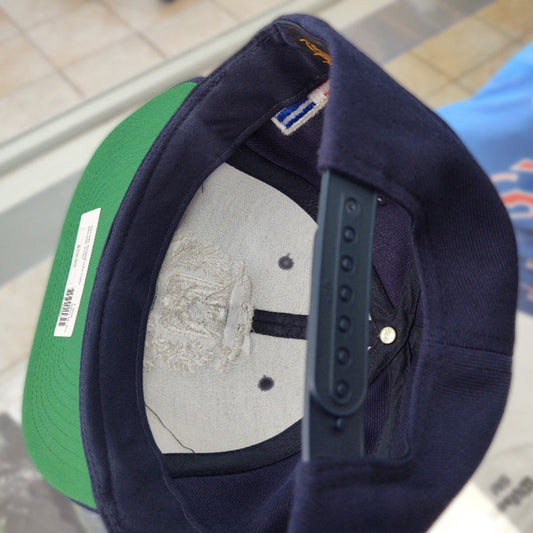 Close-up of a navy blue cap with a gray interior and green brim, on a reflective surface.
