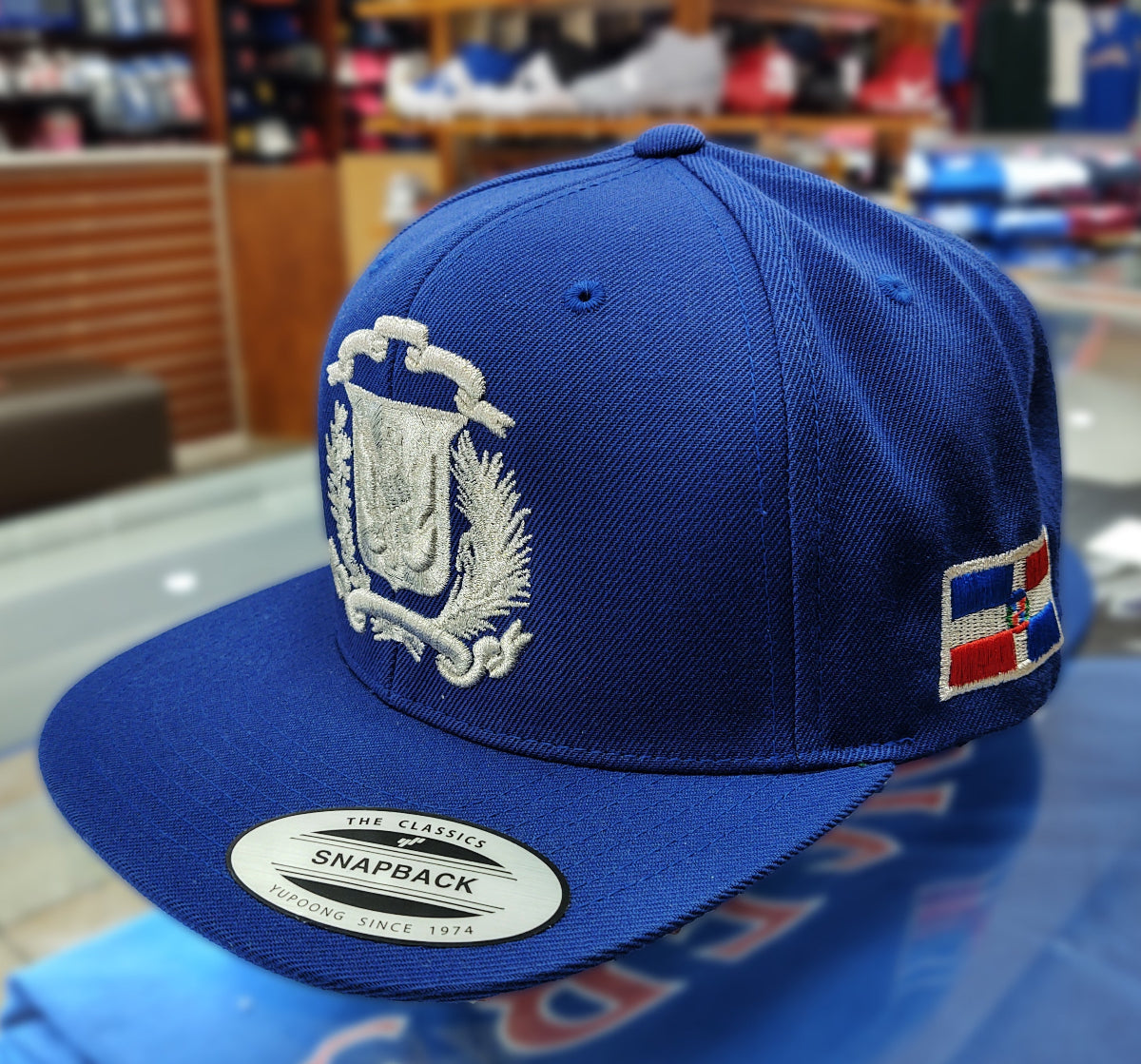 Blue snapback cap with white Dominica emblem and red, white, and blue flag patch on a reflective surface.