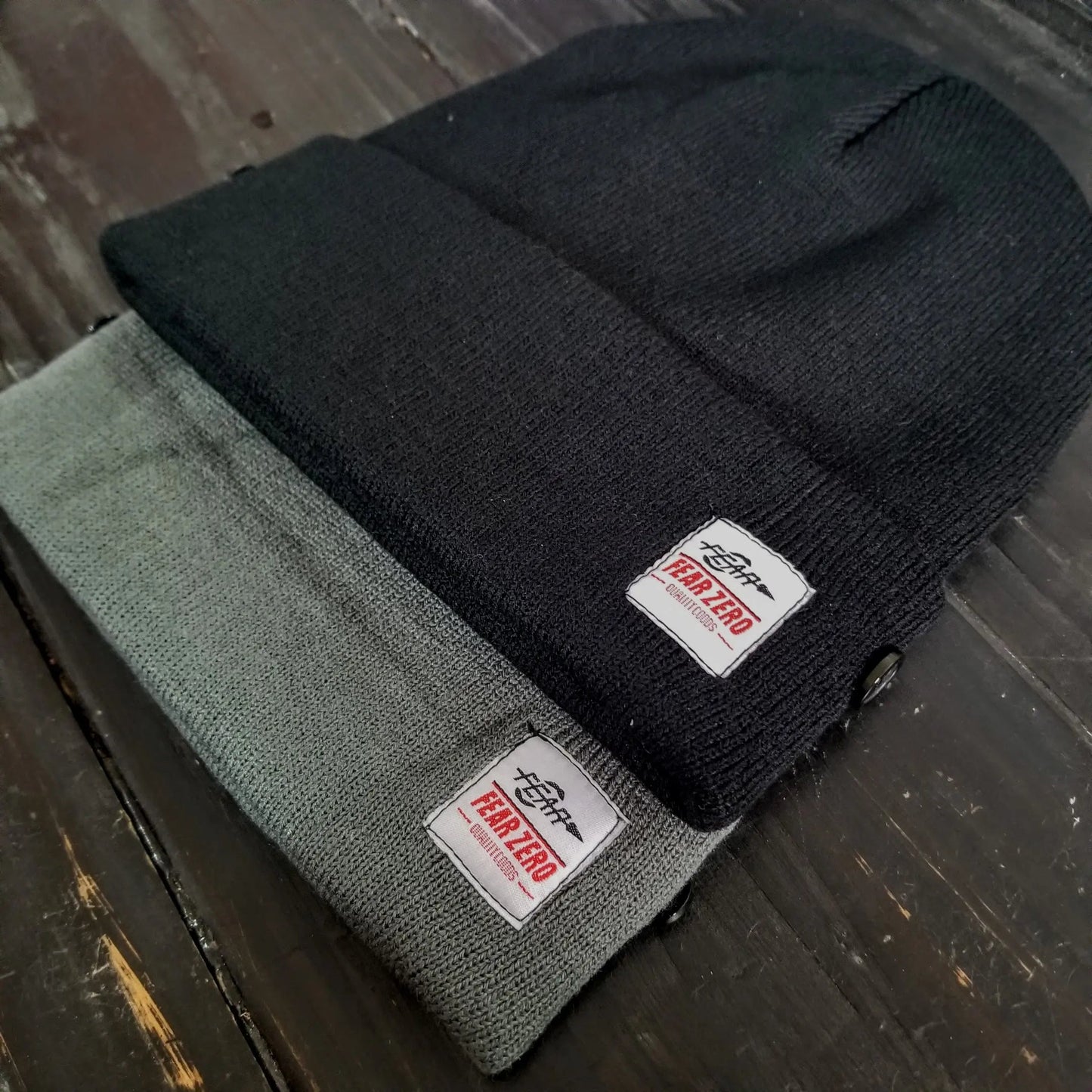 Two black beanies with Fear Zero label on a wooden surface