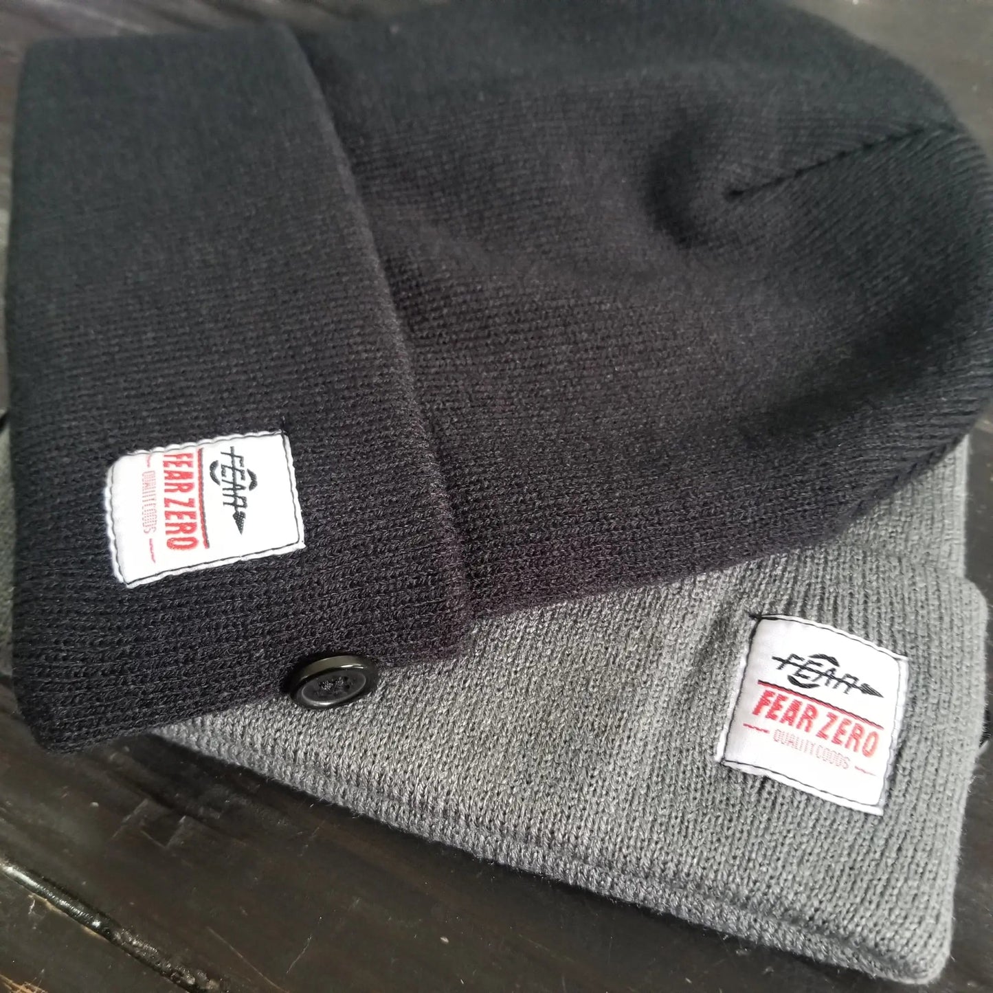 Two knit hats, one black and one gray, with 'Fear Zero' labels on a dark surface.