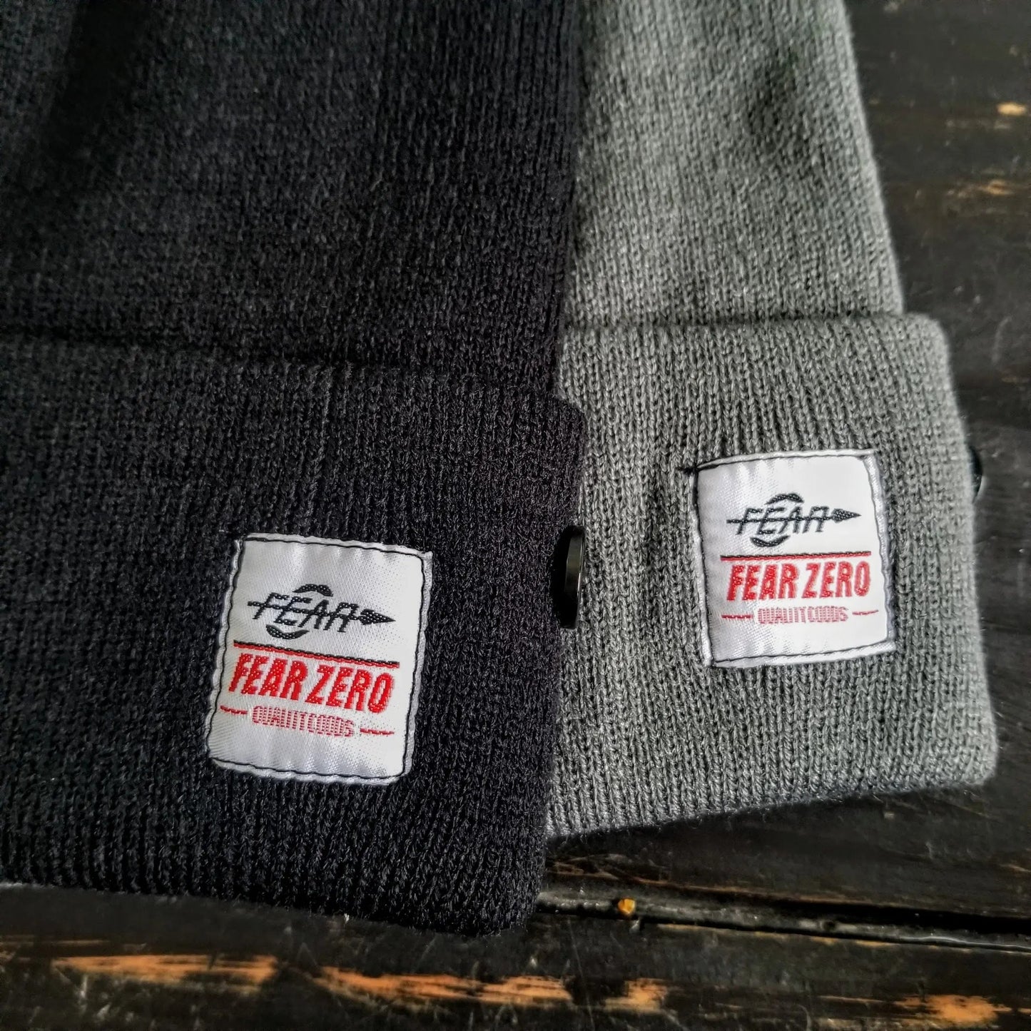 Two knit hats, one black and one gray, with 'FEAR ZERO' labels on a dark surface.