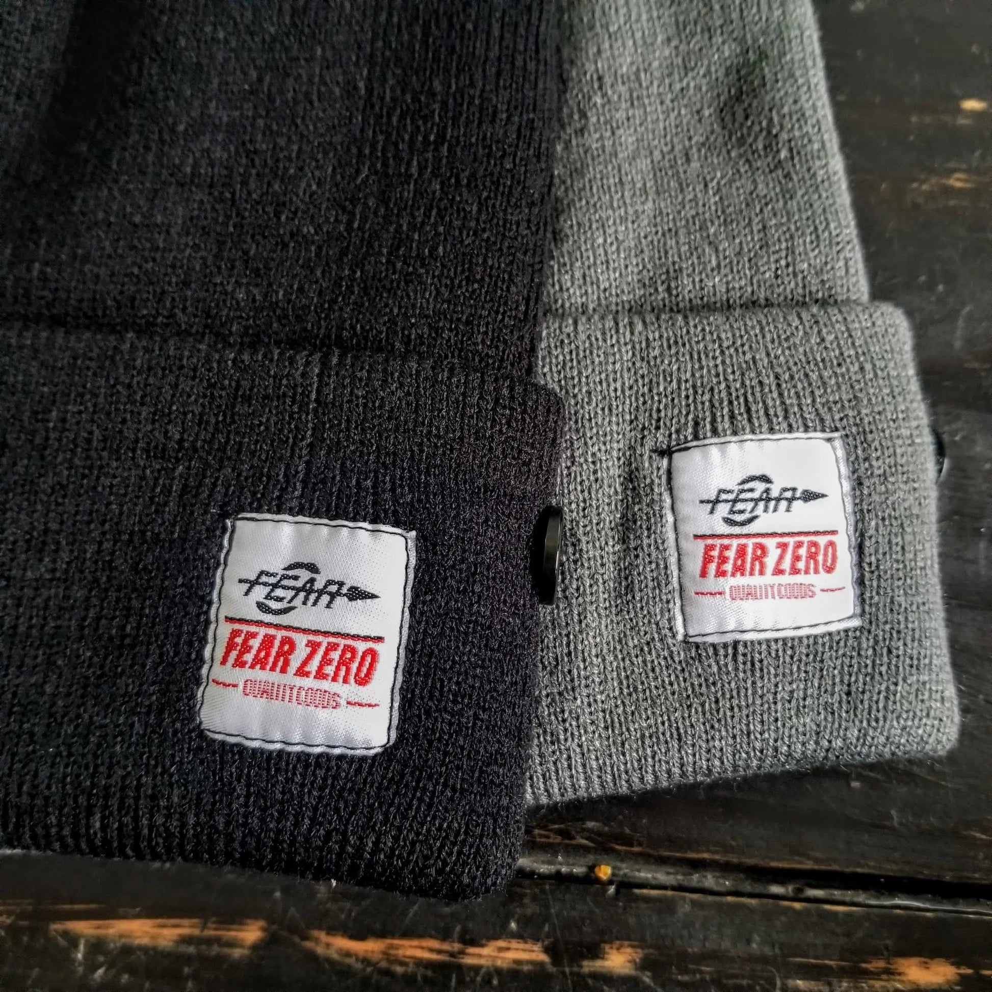 Two knit hats, one black and one gray, with 'FEAR ZERO' labels on a dark surface.