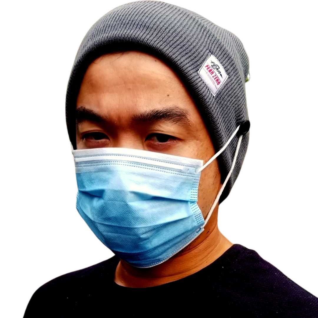 Person wearing a gray beanie and blue surgical mask on a white background