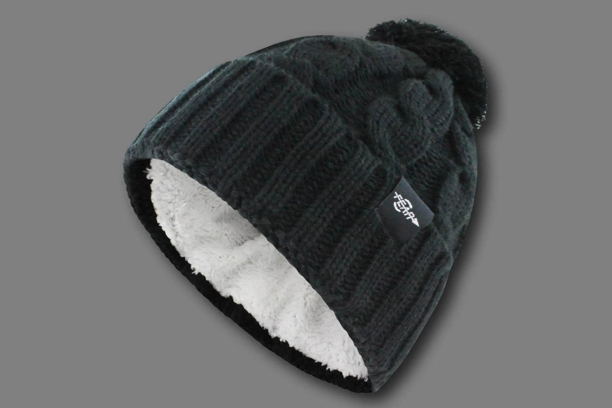 Knit beanie with white lining and pom-pom on a gray background