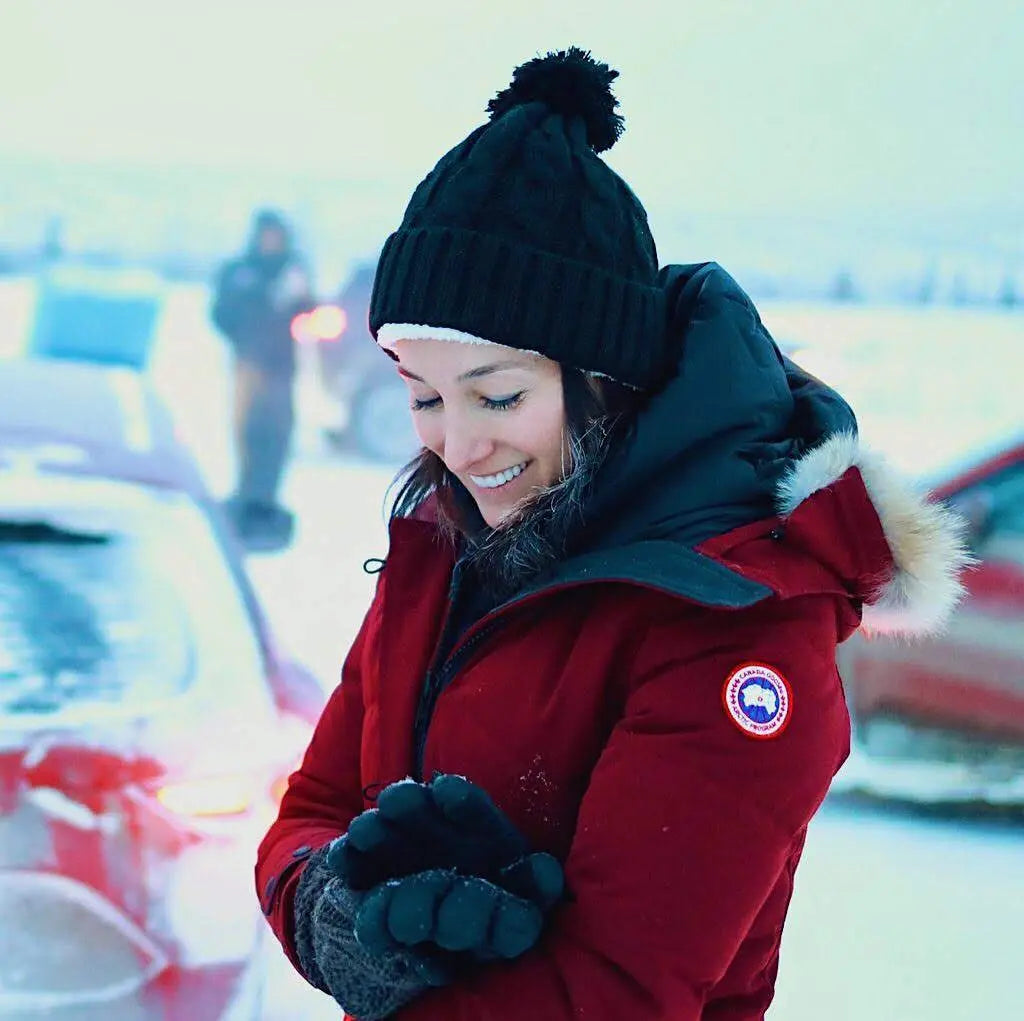 Person wearing a red coat with a brand logo, black beanie, and gloves in a snowy setting.