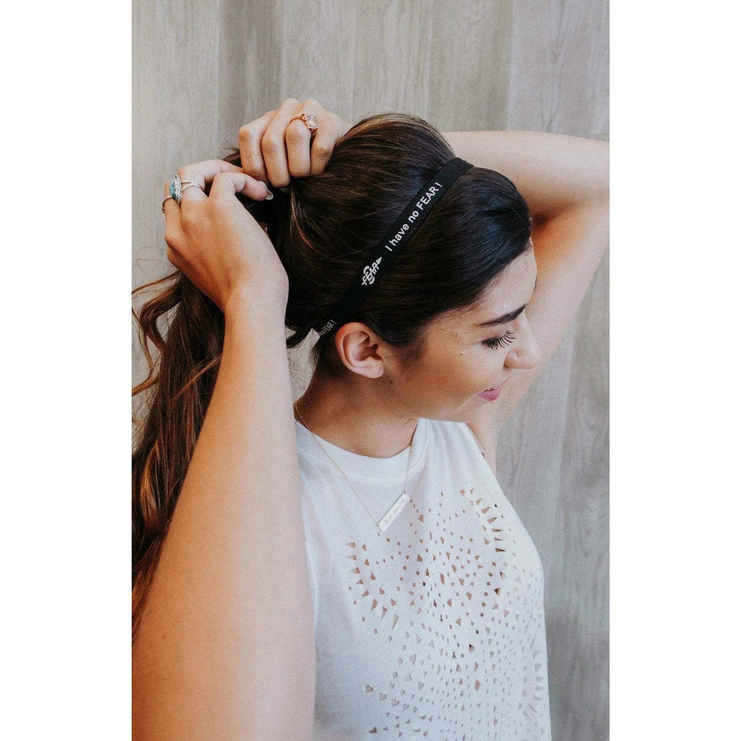 Woman wearing a headband with text, adjusting her hair against a neutral background