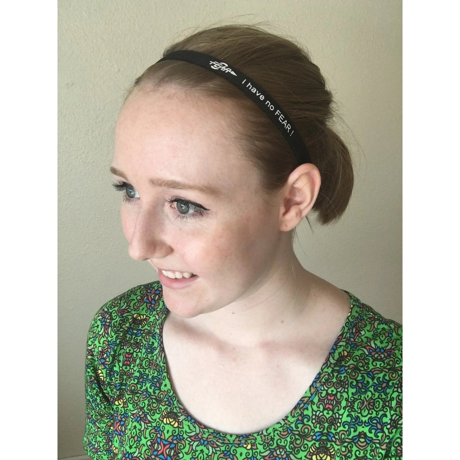 Woman wearing a green patterned top with a headband that says 'I have no FEAR'.