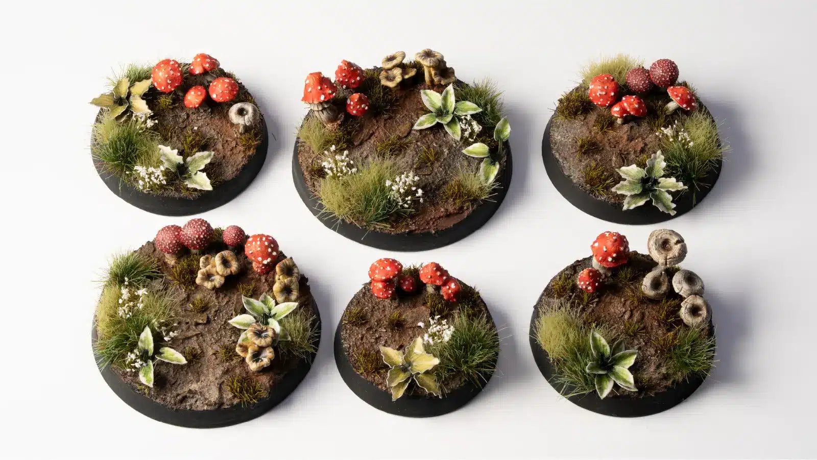 Six round miniature bases with terrain and plant decorations on a white background