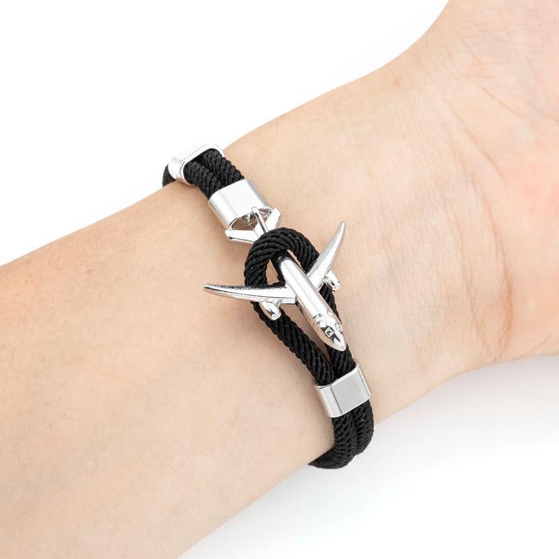 Black braided bracelet with silver airplane charm on a wrist against a white background