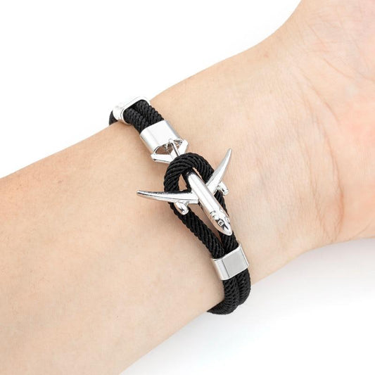 Black braided bracelet with silver airplane charm on a wrist against a white background