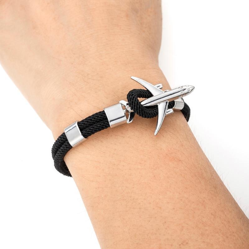 Black braided bracelet with silver anchor charm on a wrist against a white background