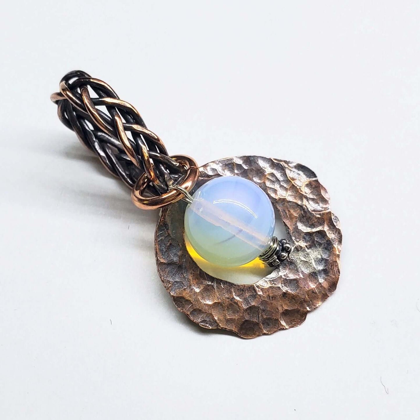 Jewelry pendant with a light blue gemstone and textured metalwork on a white background