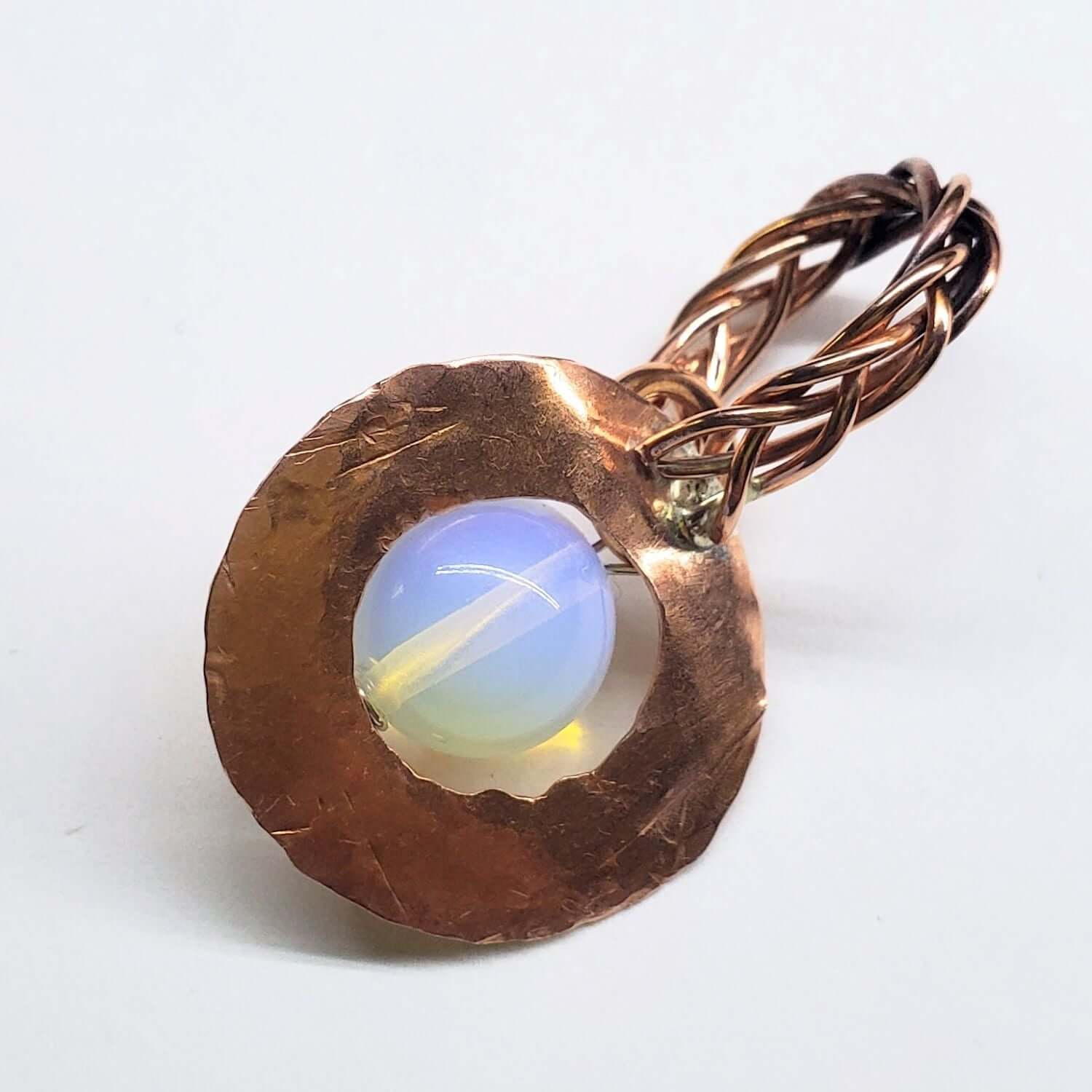 Copper tone pendant with a central opal stone on a white background