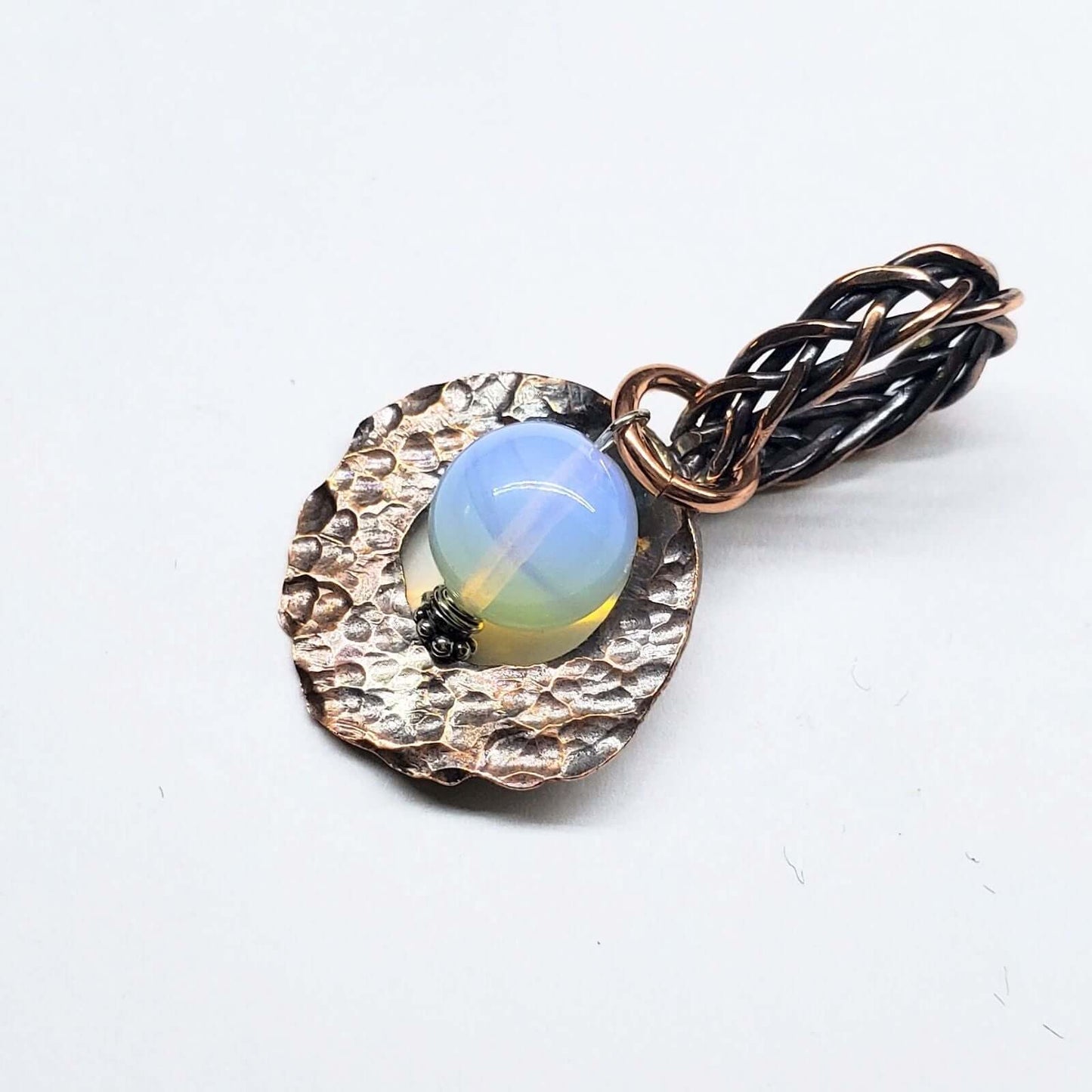 Jewelry pendant with a blue gemstone and braided design on a white background