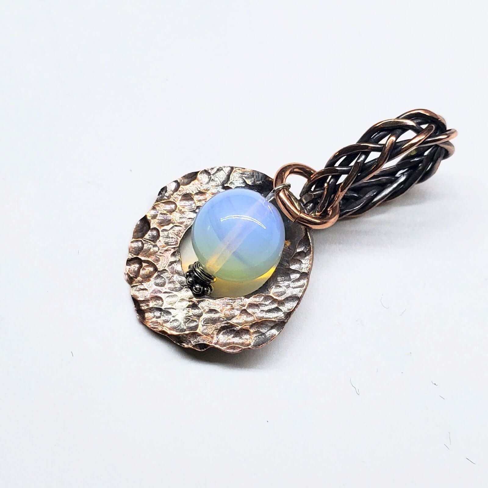 Jewelry pendant with a blue gemstone and braided design on a white background