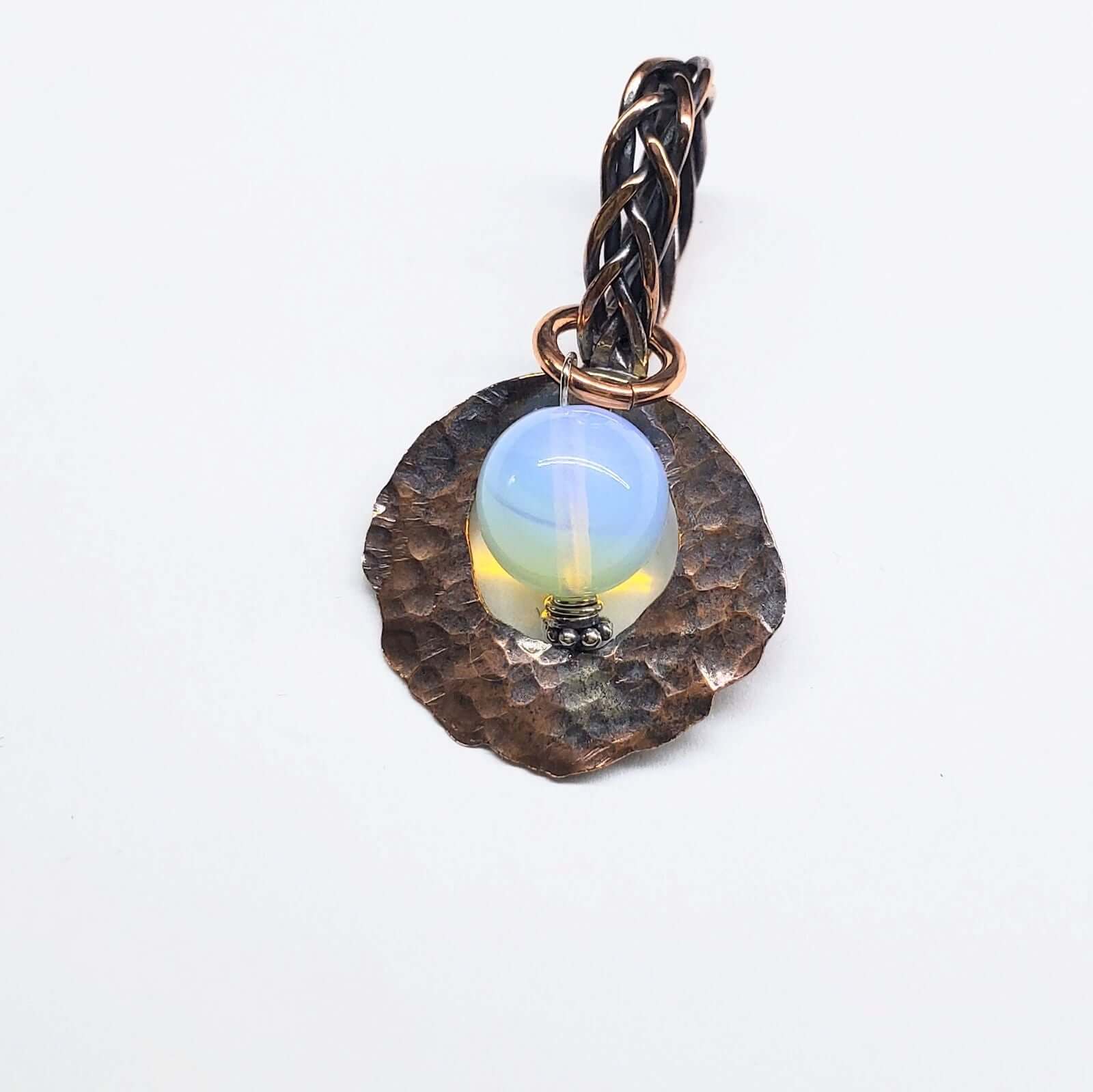 Jewelry pendant with a blue stone and braided design on a white background