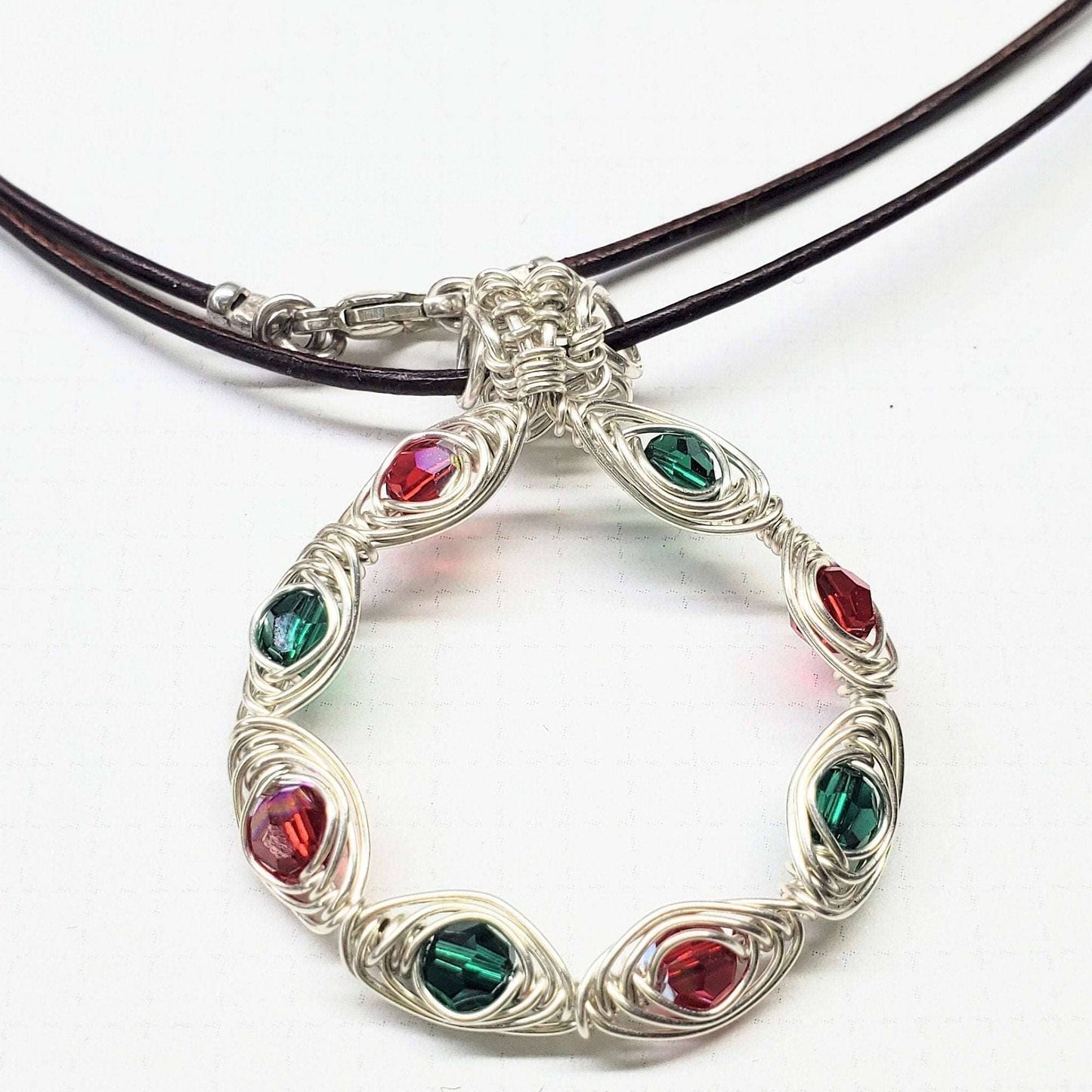 Silver necklace with circular pendant featuring red and green gemstones on a white background