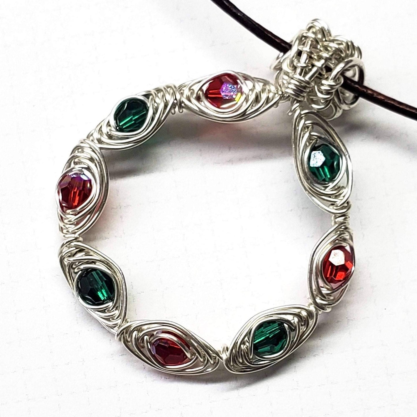 Silver circular pendant with red and green gemstones on a white background