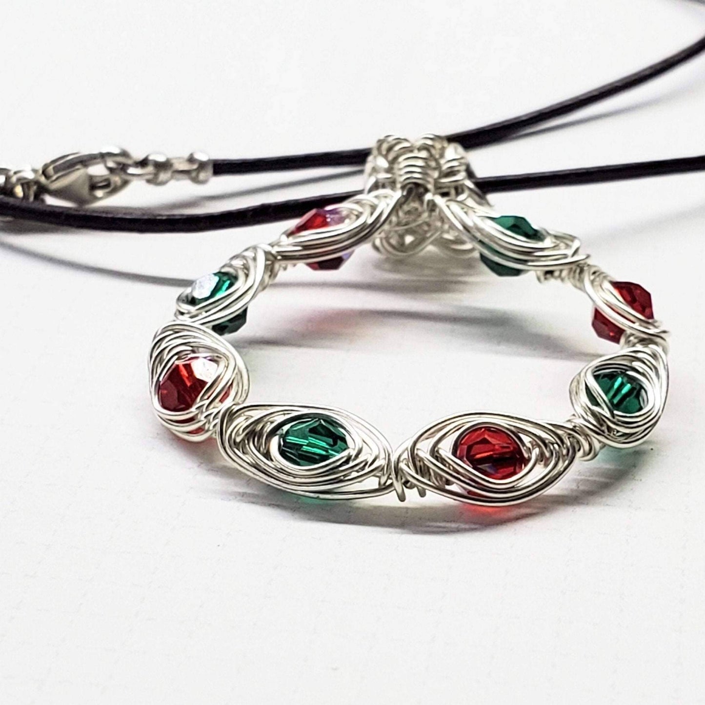 Silver bracelet with red and green gemstones on a white background