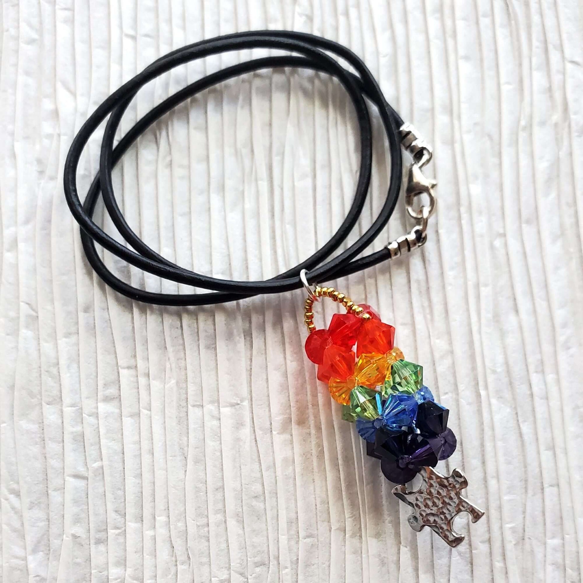 Necklace with rainbow charm and puzzle piece on a textured white surface