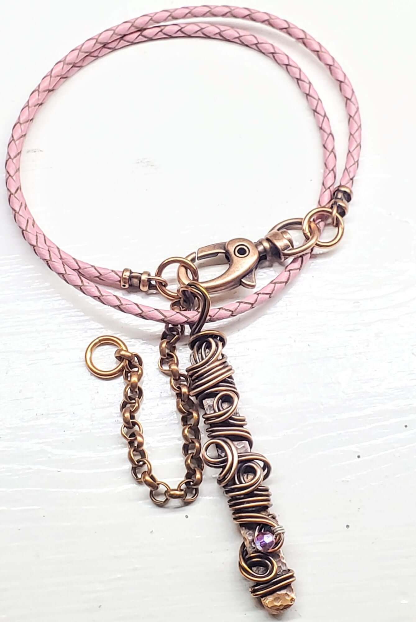Pink braided leather bracelet with a bronze wire-wrapped charm on a white background