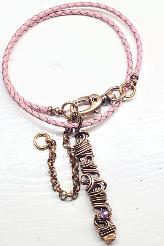 Pink braided leather bracelet with a bronze wire-wrapped charm on a white background