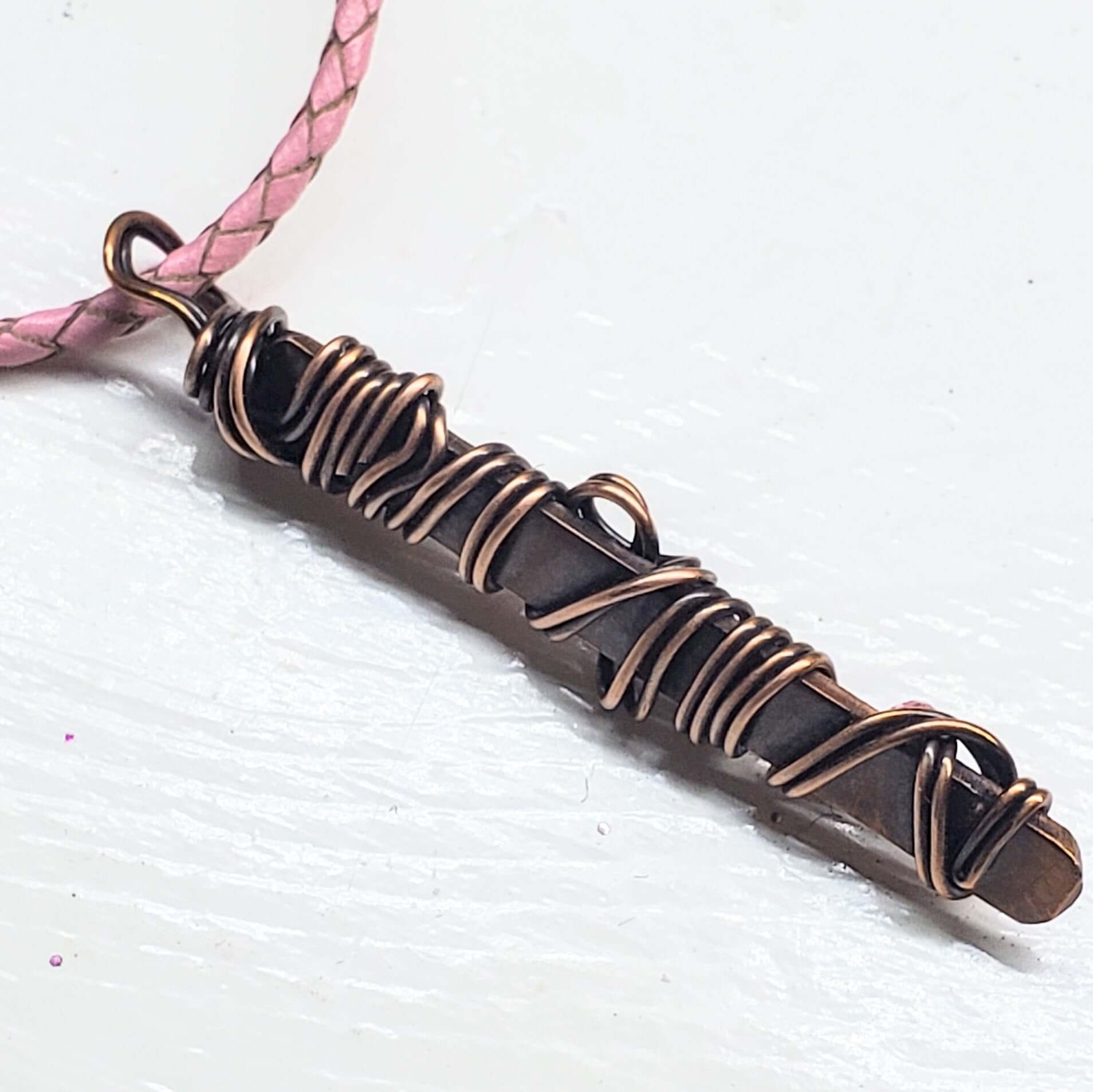 Copper-wrapped pendant on a pink cord against a white background