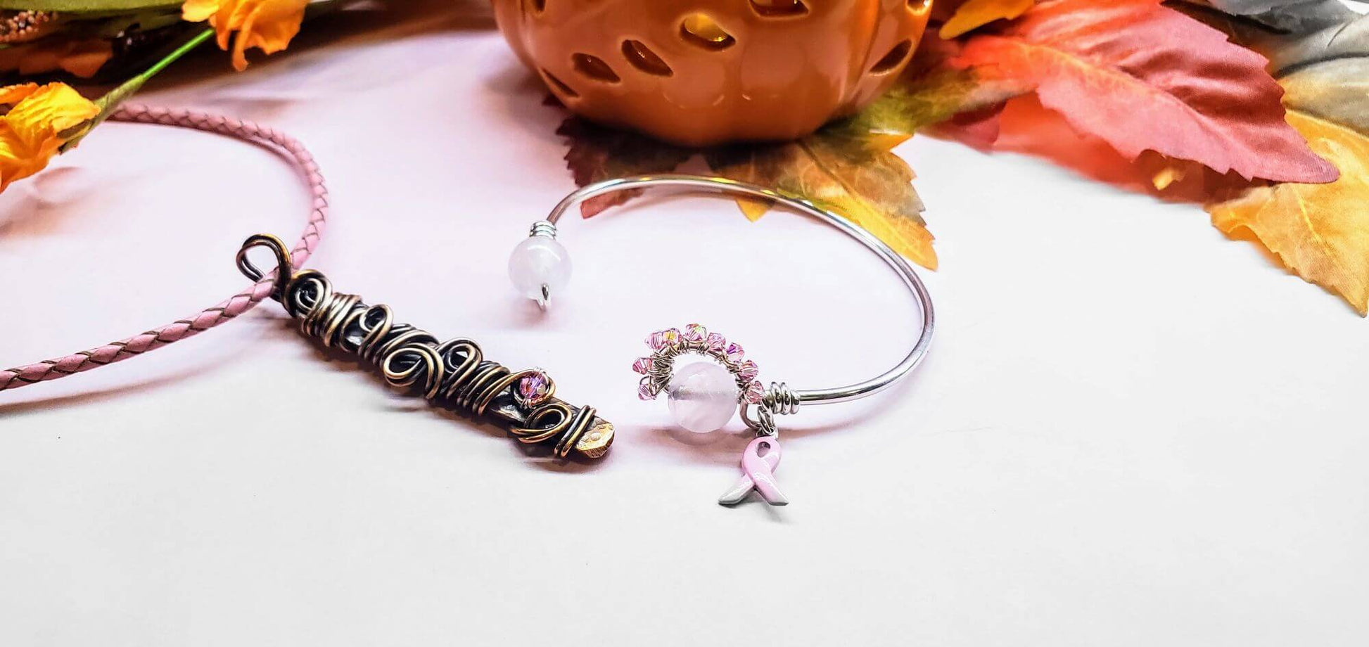 Necklace and bracelet on a white surface with autumn leaves and a pumpkin in the background