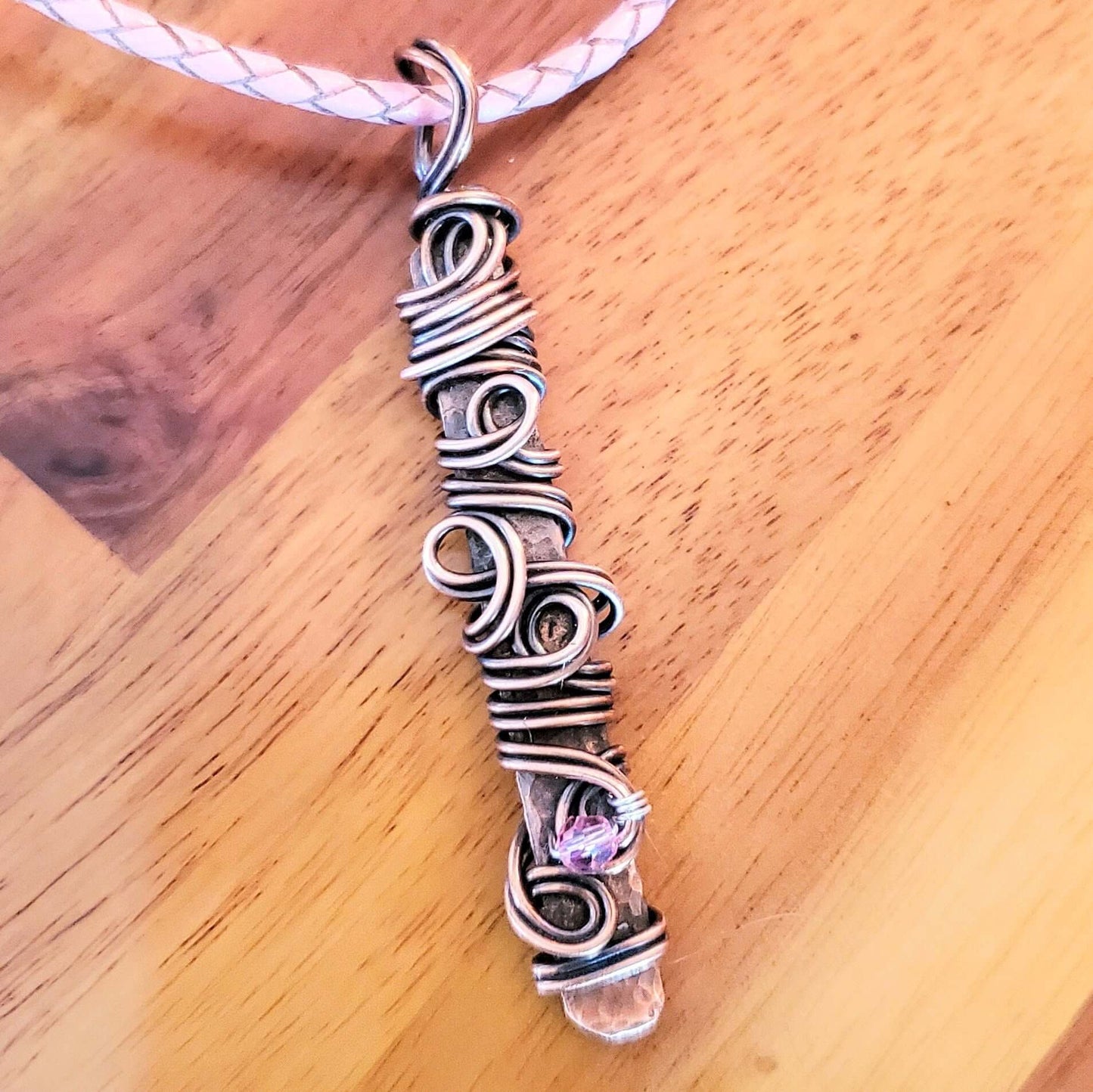 Silver wire-wrapped pendant with a pink gemstone on a wooden surface