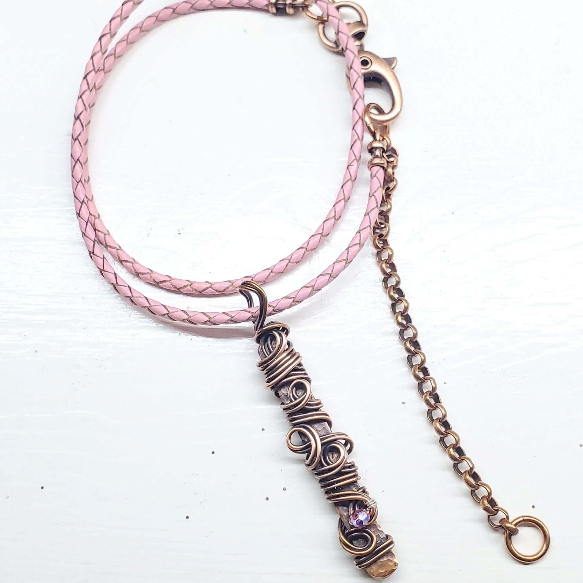 Necklace with pink braided cord and bronze pendant on a white background
