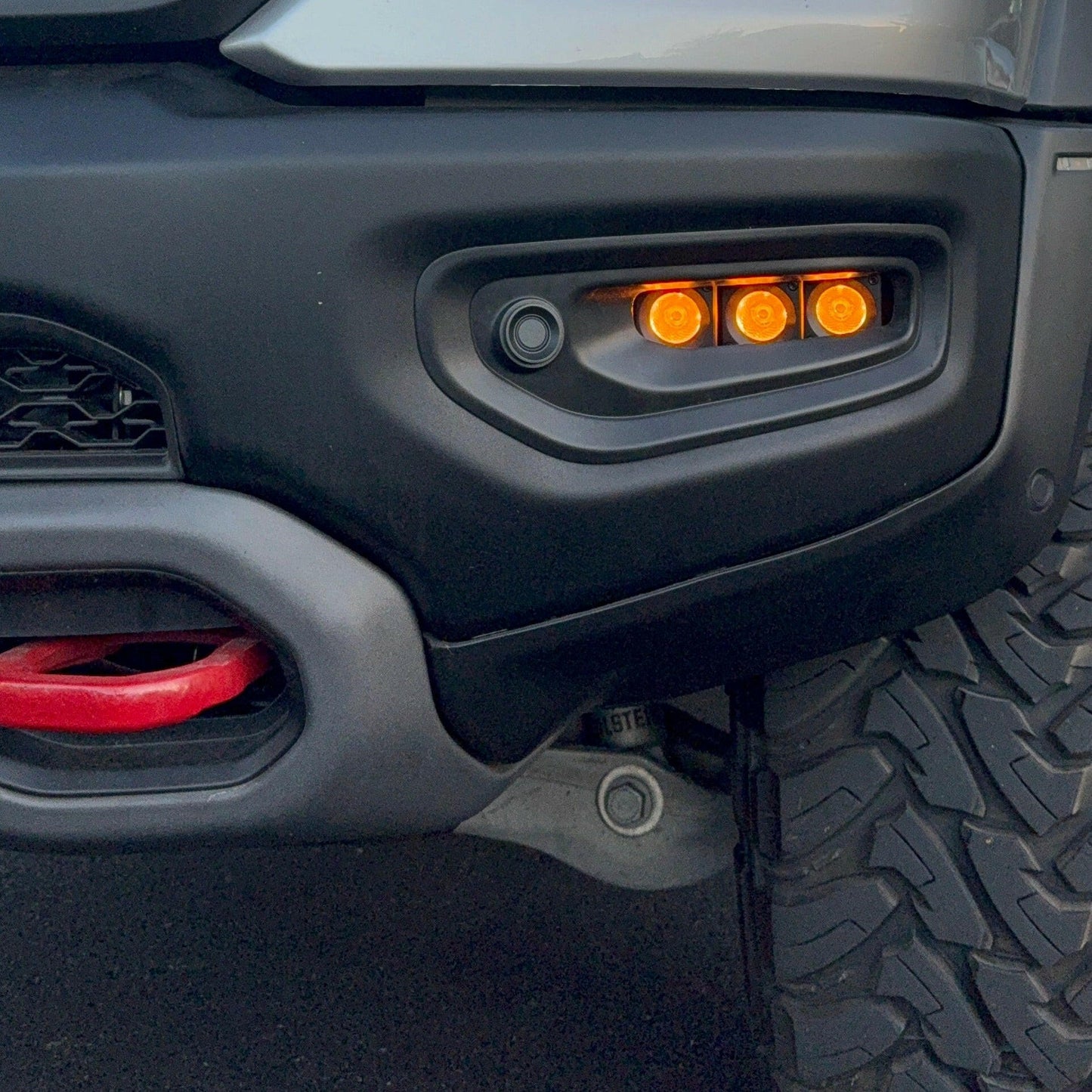 Close-up of a vehicle's front bumper with fog lights and tire tread.