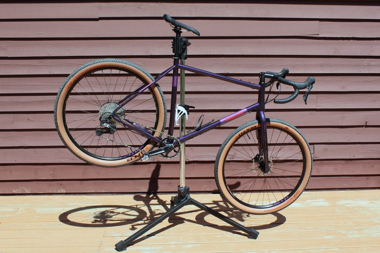 Purple bicycle on a stand against a wooden wall