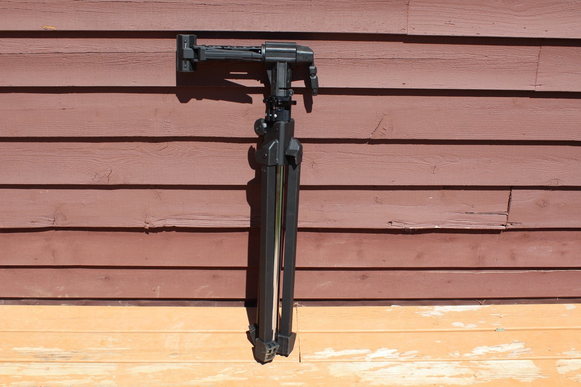 Black tripod against a wooden wall