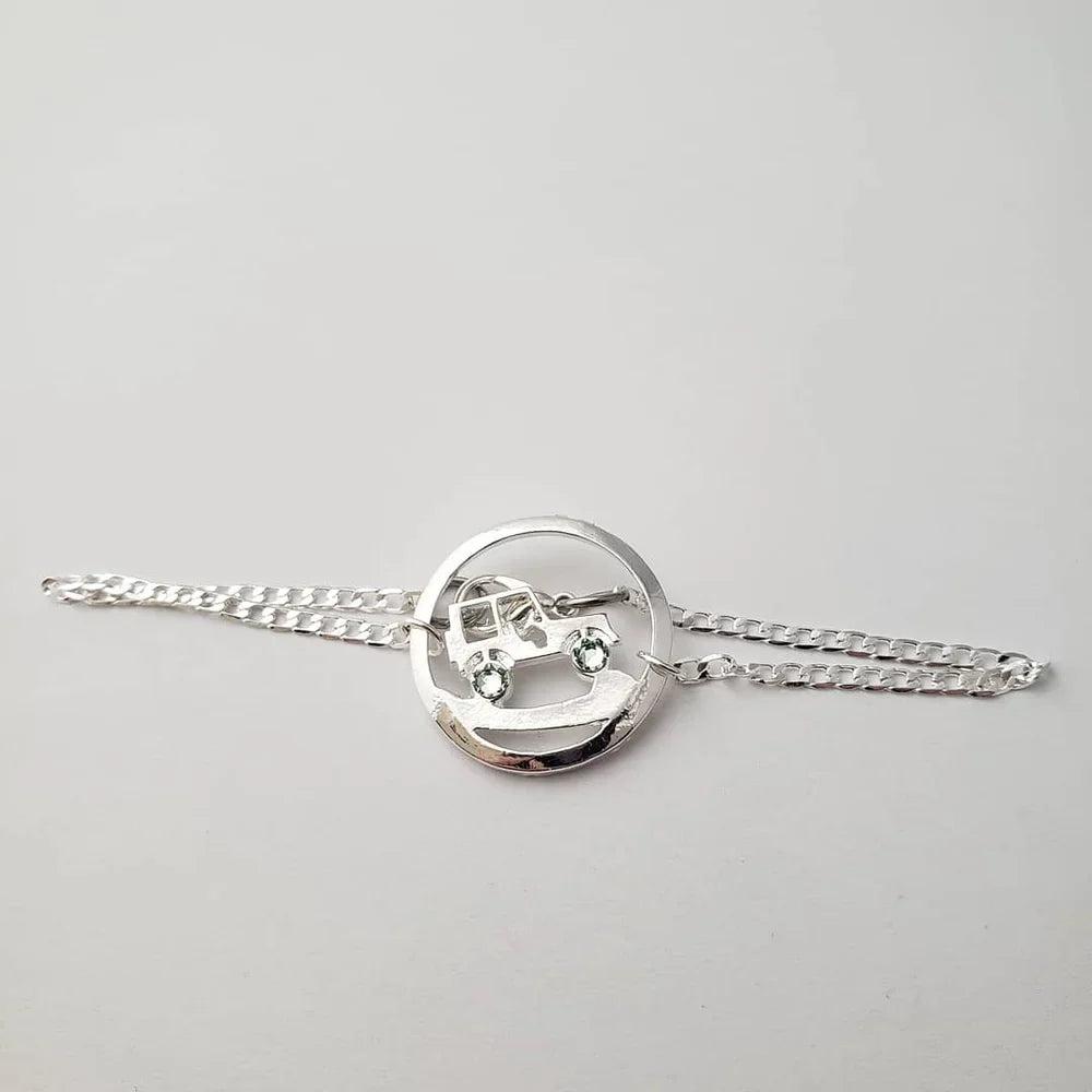 Silver bracelet with a circular jeep charm on a light gray background