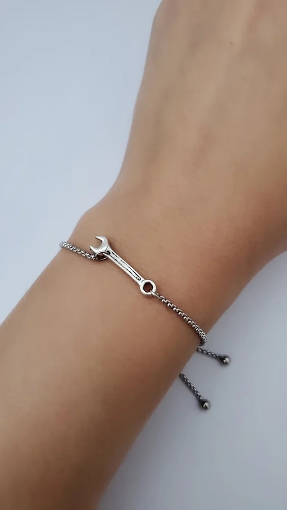 Silver bracelet with a wrench charm on a wrist against a light background