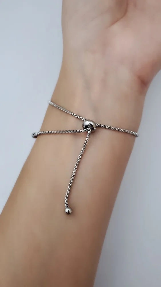 Silver bracelet with a small ball charm on a wrist against a light background